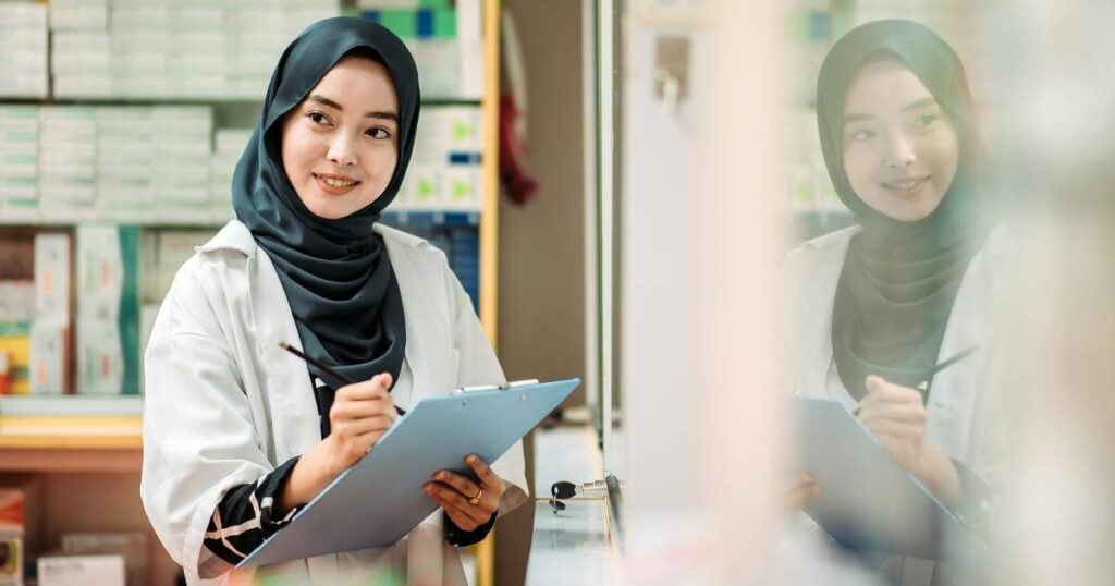 muslim female pharmacist wearing head scarf and taking notes on clipboard 