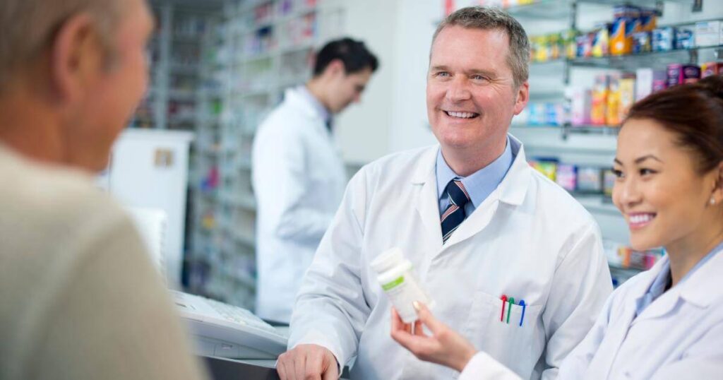 smiling pharmacy manager with technician talking to patient